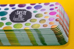 28 pt cold foil business cards with colorful polka dots and "Taste the Feeling" in a purple circle