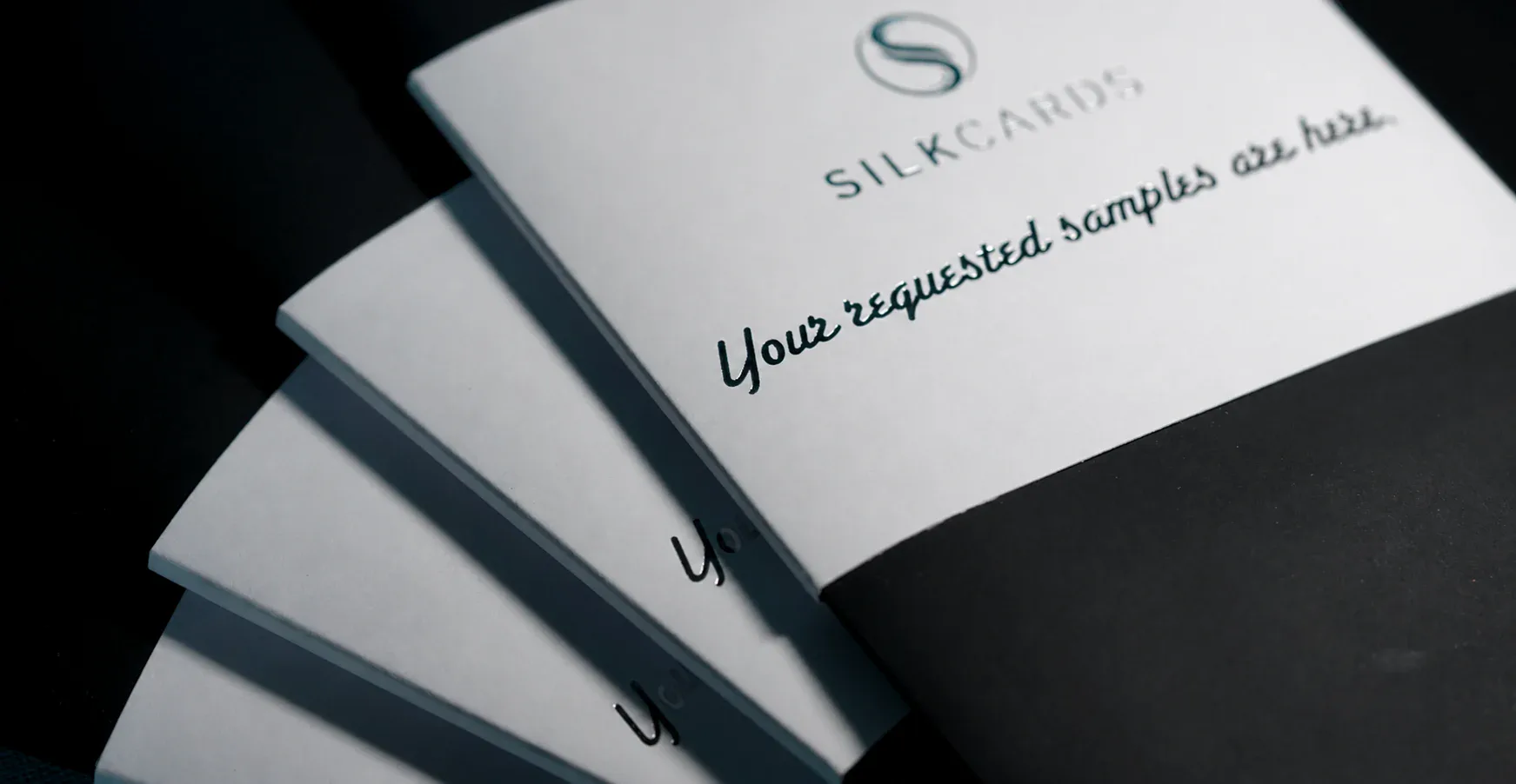 A fanned stack of SilkCards sample folders on a dark surface, the top one reading “Your requested samples are here.”